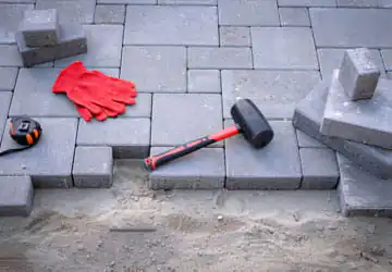 Pavers mid installation with red hammer, gloves and tape measure
